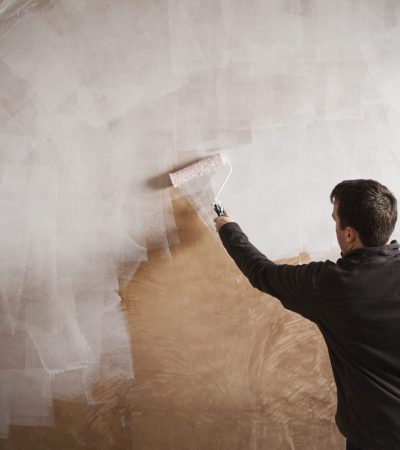 A builder, a painter holding a paint roll, painting a wall with white paint.