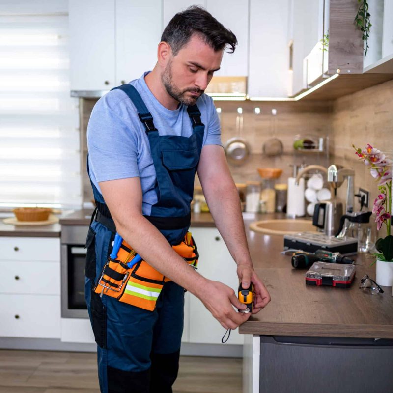 Skilled worker conducting repairs in a modern kitchen environment A worker focuses on repairs in a bright kitchen, surrounded by tools and equipment.